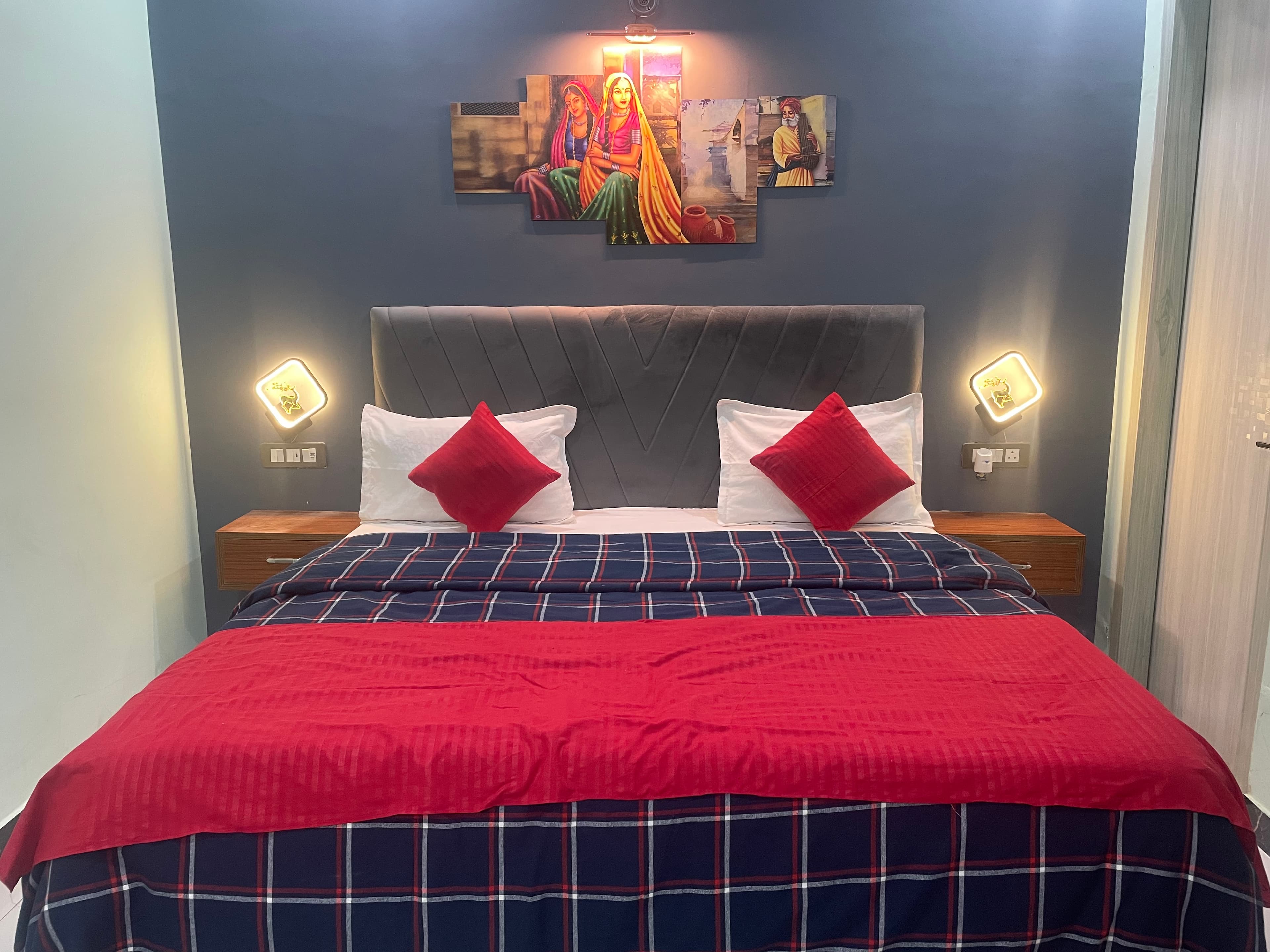 King bed with red checkered linen, velvet headboard and Rajasthani art panels