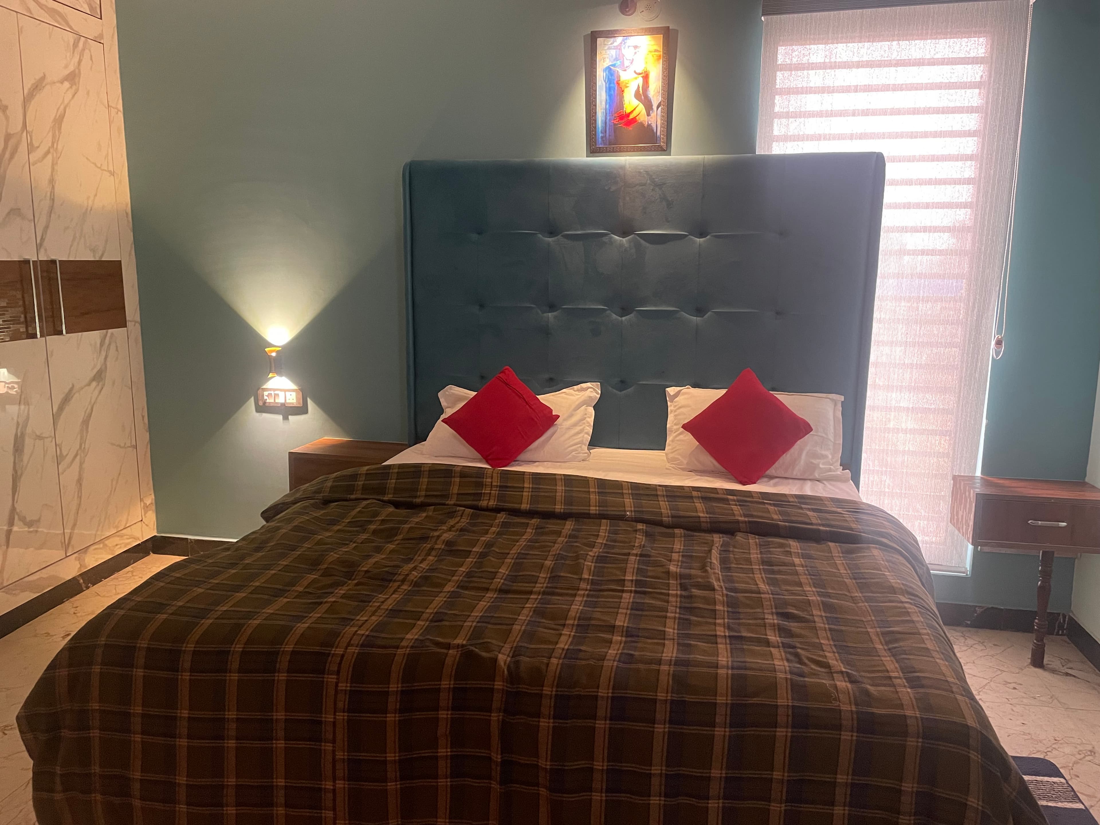 Teal Deluxe room — tufted blue headboard with olive plaid bedding and red accent pillows